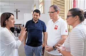Drei Caritas-Mitarbeitende aus Deutschland stehen zusammen und hören dem Vortrag einer Caritas-Mitarbeiterin aus Havanna (Kuba) zu