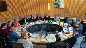 Vertreter/innen der Grünen Landtagsfraktion NRW und Direktorinnen der fünf Diözesan-Caritasverbände in NRW sitzen an einem runden Sitzungtisch in einem Konferenzraum des Düsseldorfer Landtags zusammen
