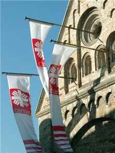 Der obere Teil eines Kirchengebäudes an dem, an langen Metallstangen, drei Caritasflaggen runterhängen