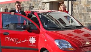 Peter Biesenbach (CDU) steht zwischen der geöffneten Tür eines roten Pflegeautos. Auf der anderen Seite des Autos steht eine weibliche Pflegekraft.
