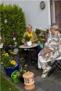 Zwei Bewohnerinnen des Rohlandshofes sitzen auf einer Terrasse im Garten und unterhalten sich.