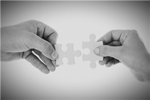 Schwarz-weiß-Bild von zwei Händen, die weiße Puzzleteile zusammenführen.
