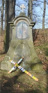 Holzkreuz vor einem Steindenkmal
