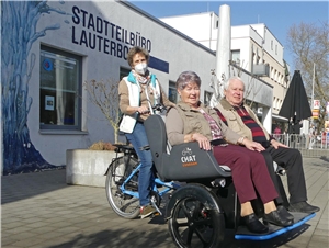 Quartiersmanagerin fährt zwei Senioren auf der Rikscha spazieren