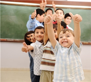 Fröhliche Kinder im Klassenzimmer, die ihre Daumen hochstrecken