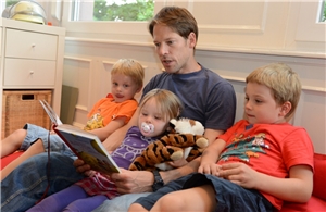 Unternehmensservice Vater liest drei Kindern ein Buch vor.