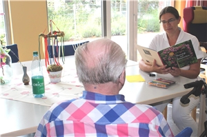 Altenpflegerin Pia Warnecke liest einem Besucher der Tagespflege vor. Tagespflege St. Josefspflege