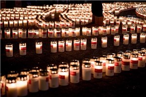 Man sieht sehr viele Kerzen die im dunkeln Leuchten und im Flammenkreuz des Caritas Logos angeordnet sind
