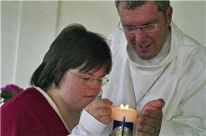 Seelsorger und eine Frau mit Behinderung zünden eine Kerze an