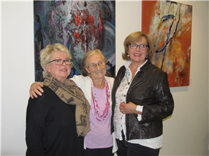 Drei Frauen stehen vor Bildern in einem Ausstellungsraum.