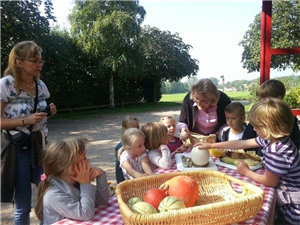 Kinder stehen um einen Tisch mit verschiedenen Lebensmitteln. Eine Frau hält ein ei in der Hand und erklärt den Kindern dazu.