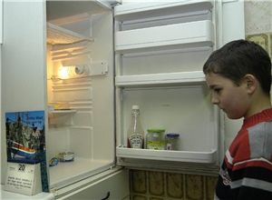 Kleiner Junge steht vor einem geöffneten Kühlschrank.