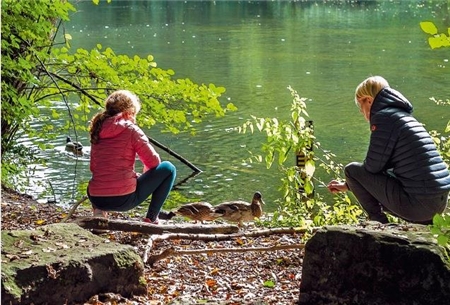 Lernpatin und Schülerin betrachten am Seeufer eine Ente.
