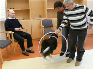 ein Mann hält einen Reifen, durch den ein Hund springt