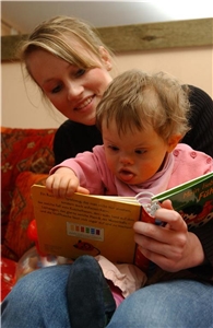 junge Frau schaut mit Kleinkind mit Behinderung ein Bilderbuch an