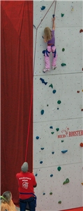 Ein Kind klettert gesichert von einen Betreuer eine Kletterwand hoch