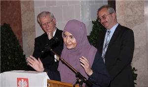 Eine junge muslimische Mutter spricht nun ins Mikrofon. Sie trägt ein violettes Kopftuch. Hinter ihr stehen Prof. Stande und unser Caritasdirektor. 