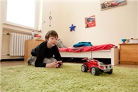 Haus Nazareth Leverkusen Ein Junge liegt auf dem Bauch auf dem Boden und guckt sein Spielzeugauto an