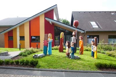 Stiftung_Die_Gute_Hand Blick auf den Eingang des Multifunktionsraums Prälat Freudenberg mit den bunten Holzfiguren