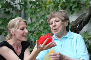 Grundsätze unserer Arbeit Eine Mitarbeiterin des Caritas-Altenzentrums Heilig Geist beschäftigt sich mit einer Bewohnerin. Die Mitarbeiterin hat ein rotes Tuch in der Hand zusammengeknüllt, das sich langsam entfaltet. Die Bewohnerin verfolgt die Bewegungen des Tuchs.