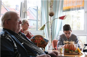 Bewohner sitzen in gemütlicher Runde mit einem jungen Mann am Tisch. Er liest ihnen vor. Bewohner sitzen in gemütlicher Runde mit einem jungen Mann am Tisch. Er liest ihnen vor.