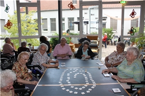 Eine Runde von Seniorinnen und Senioren sitzen rund um einen Tisch und spielen ein Gesellschaftsspiel