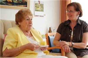 Eine ältere Dame mit einer Besucherin in ihrem Zimmer in einer Seniorenpflegeeinrichtung