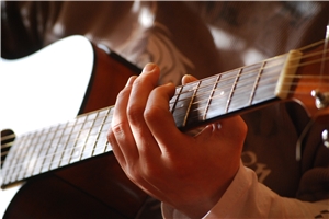 Hände umfassen eine Gitarre und spielen auf dem Instrument.