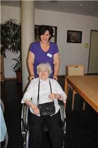 Eine Mitarbeiterin des Katholischen Altenzentrums Landau fährt eine Bewohnerin im Rollstuhl durch die Einrichtung.