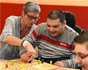 Eine Mitarbeiterin spielt mit einem Mann mit Behinderung das Würfelspiel 'Mensch ärgere dich nicht' Behinderung