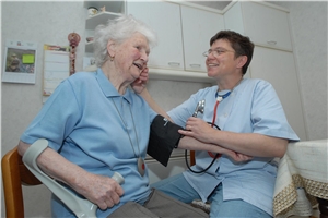 Pflegefachkraft und Seniorin beim Blutdruckmessen