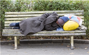 Obdachlos im Winter: Ein obdachloser Mann, mit dickem Mantel und Mütze bekleidet, liegt auf einer Parkbank.