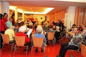 Senioren und Mitarbeiter sitzen im Kreis und singen.