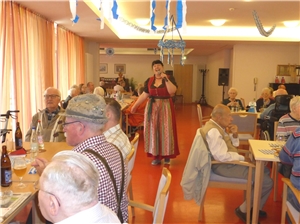 Die Frau im Dirndl geht mit dem Mikrofon singend durch die Tischreihen in der Cafeteria. Oktoberfest 4