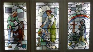 Ein großes dreigeteiltes Glasfenster zeigt verschiedene christliche Motive der Nächstenliebe. 