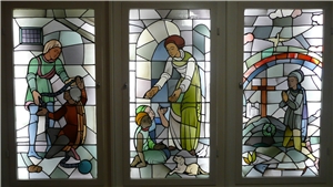Ein großes dreigeteiltes Glasfenster zeigt verschiedene christliche Motive der Nächstenliebe. Ein großes dreigeteiltes Glasfenster zeigt verschiedene christliche Motive der Nächstenliebe.