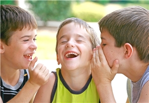 Drei Jungen, die sich etwas ins Ohr flüstern und lachen