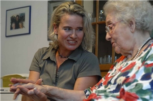 Eine ehrenamtliche Mitarbeiterin besucht eine ältere Bewohnerin eines Altenzentrums und hält ihre Hand. 