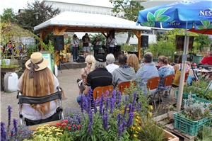 Die Besucher lauschen mitten im Grünen der Musik auf der Bühne. Hack-Garten Besucher
