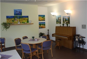 Unser Haus Aufenthaltsraum mit Stühlen, Tischen und einem Klavier.