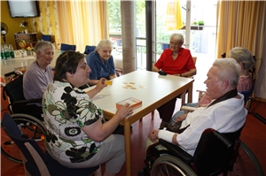 Die Bewohner sitzen mit einer Mitarbeiterin am Tisch und spielen ein Ratespiel. Die Bewohner sitzen mit einer Mitarbeiterin am Tisch und spielen ein Ratespiel.