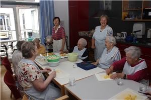 Bewohnerinnen des Caritas-Altenzentrums St. Josefspflege sitzen an einem großen Tisch und schälen Kartoffeln. Tagespflege
