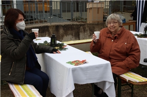 Leiterin Gudrun Wolter (links) und eine Bewohnerin sitzen auf Bänken an einem weißgedeckten Tisch und trinken Punsch