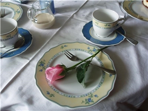 Ein festlich gedeckterTisch mit weißer Tischdecke und feinem Porzellan. Auf dem Teller liegt eine Rose.