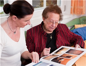 Eine Mitarbeiterin der Altenpflege blättert mit einer Bewohnerin in einem Bildband. 