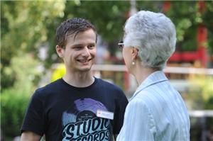 Junger Mann spricht freundlich lachend mit älterer Frau, eine Bewohnerin eines Altenzentrums. 