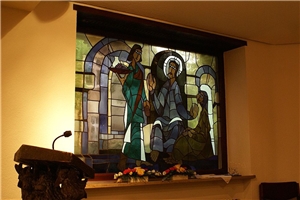 Das Fenster in der Kapelle vom Altenzentrum St. Martha mit buntem Glas, das eine Szene aus dem Neuen Testament mit Jesus Christus und einem Mann und einer Frau an seiner Seite zeigt.