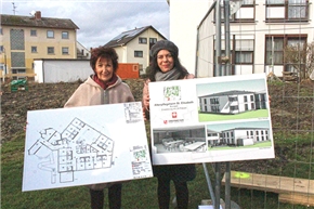 Bürgermeinsterin Bärbel Schader und Caritasdirektorin Stefanie Rhein mit den Plänen für den Neubau. Zwei Frauen vor Baugelände, eine hält einen Bauplan, die andere eine Grafik mit Abbildungen des fertigzustellenden Gebäudeanbaus