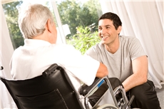 Junger Mann unterhält sich mit Senior im Rollstuhl