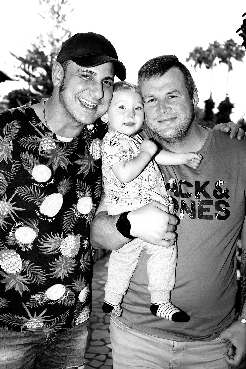 Schwarz-weiß Bild von zwei Männern, einer trägt ein Kleinkind auf dem Arm. 